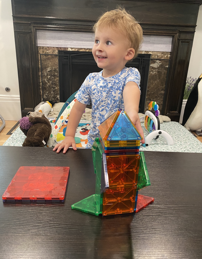 Toddler proudly presenting a tower from magnetic tiles