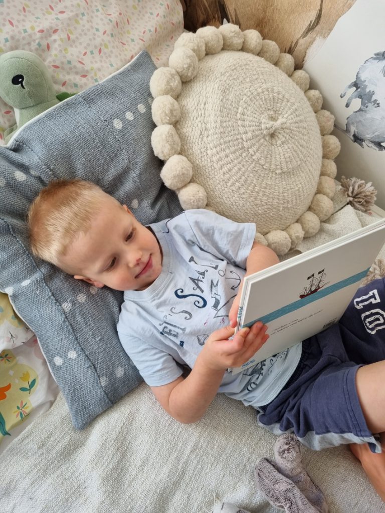 Child reading a book in a montessori floor bed.