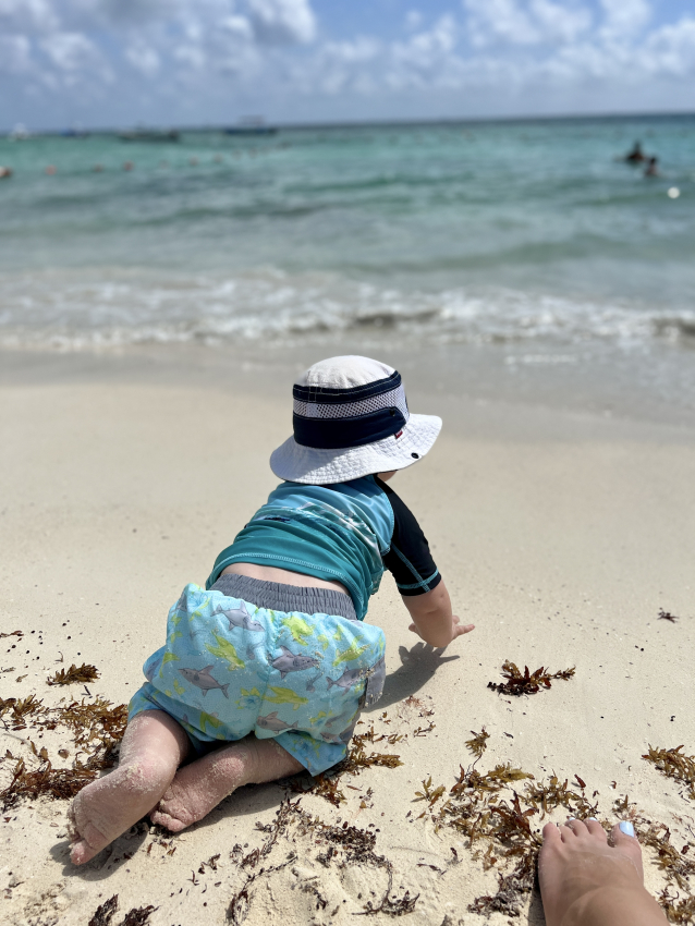 Baby crawling on a beach in swim trunks with in-built swim diaper.