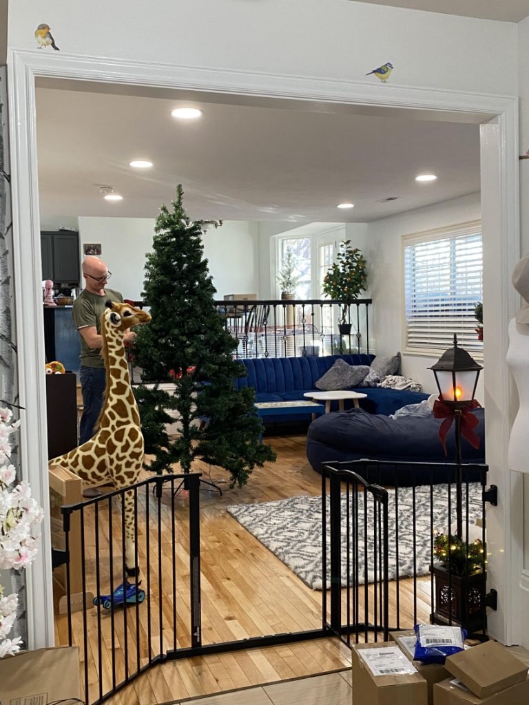 Baby gate enclosing the living room area where man is decorating tree.