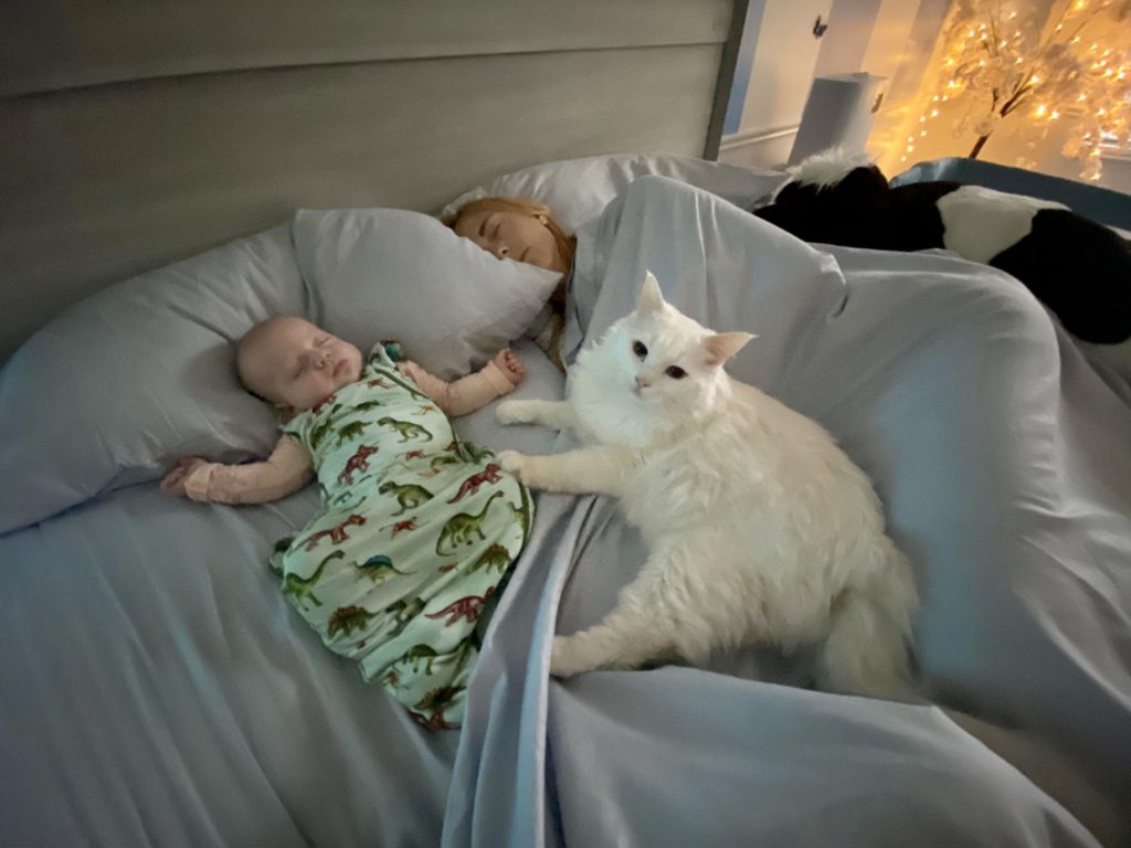Child in a green sleep sack next to his mother and a cat.