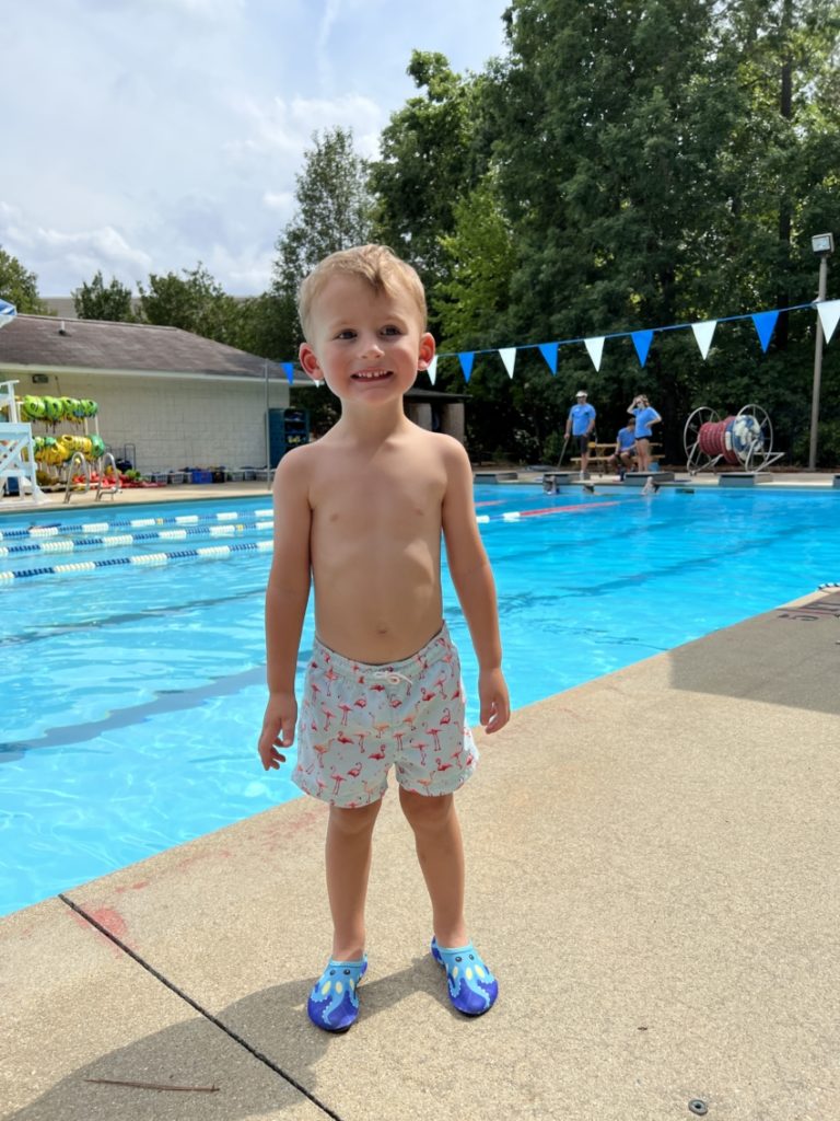 Young boy wearing blue water shoes / water socks next to a pool.