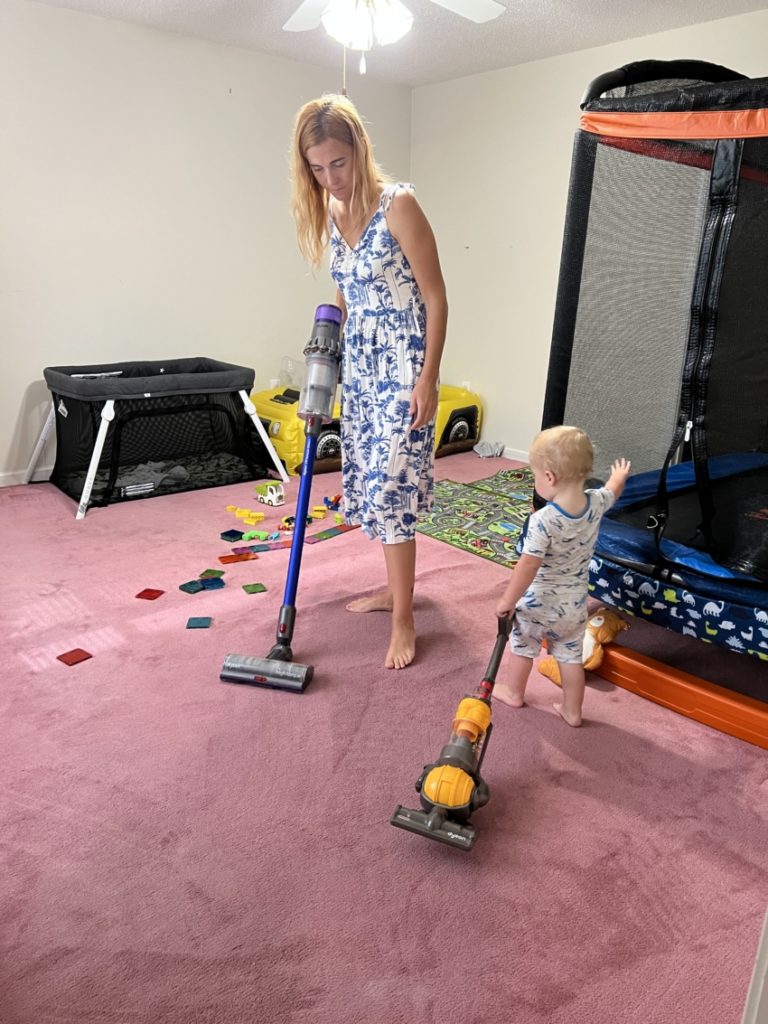 Toddler helping to vacuum using a toy vacuum